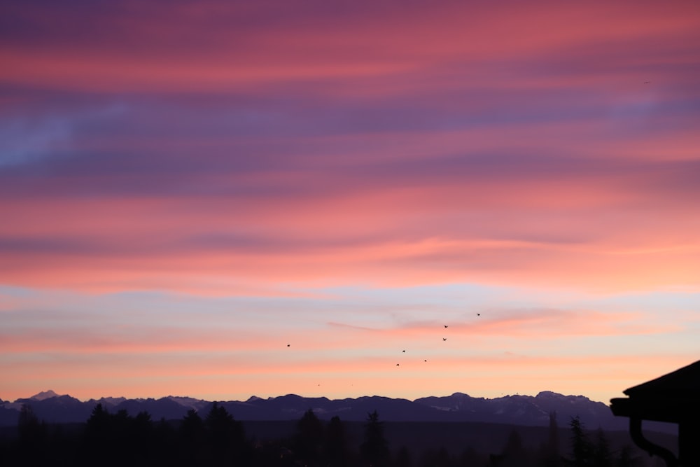 a sunset view of a mountain range with birds flying in the sky
