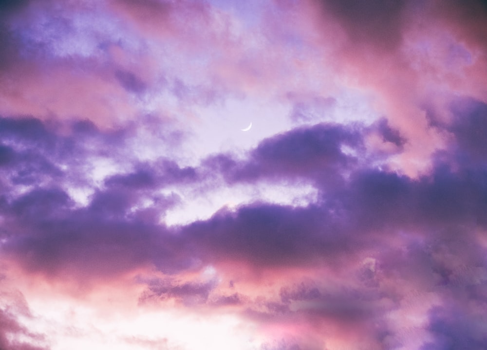 a plane flying through a cloudy sky with a moon in the distance