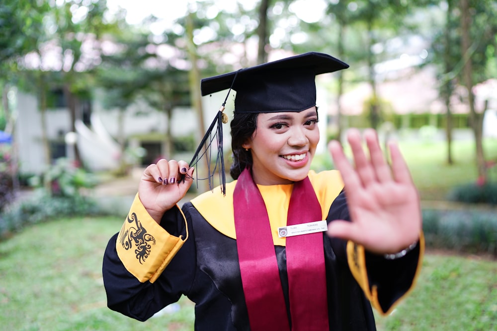 a woman wearing a graduation gown and holding her hand up