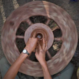 An artisan shaping clay on a potter’s wheel with city skyline blurred in the background.