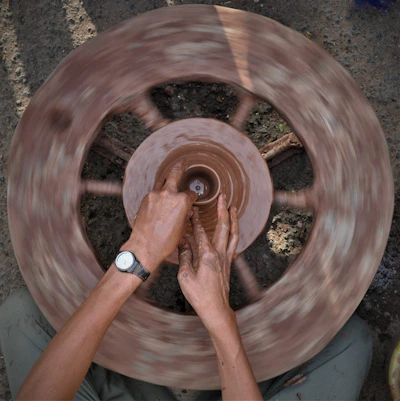 Hands shaping a clay pot on a spinning wheel, surrounded by soft natural light.