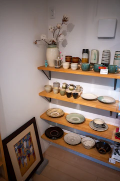 A curated shelf displaying ceramics, books, and small plants.