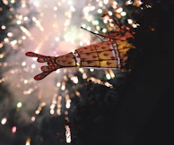 Colorful fireworks exploding above a lively mehndi event with guests enjoying under glowing lanterns.