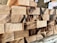 A stack of neatly arranged rectangular wooden blocks, some with dark burn marks and a smooth, polished texture. The background features an out-of-focus setting suggesting an indoor workshop environment.