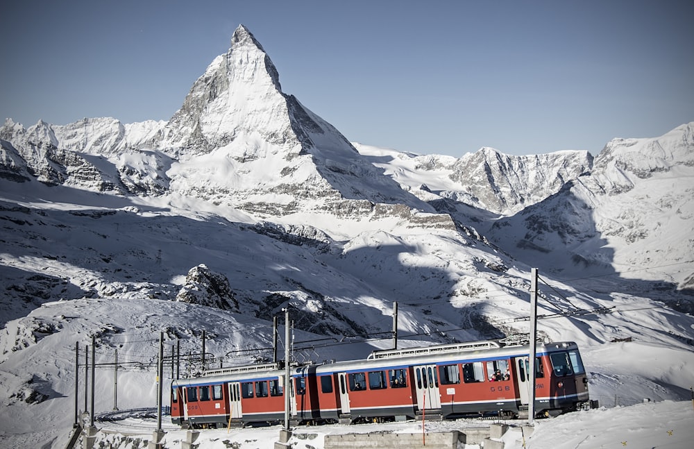 a red and blue train traveling past a snow covered mountain