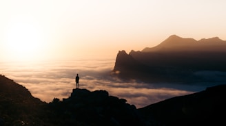 A solo traveler standing on a mountain peak, gazing at a vast valley below during golden hour.
