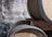 Several wooden barrels are stacked against a rustic, textured wall. One of the barrels has a small device attached to it, which appears to be a fermentation airlock.