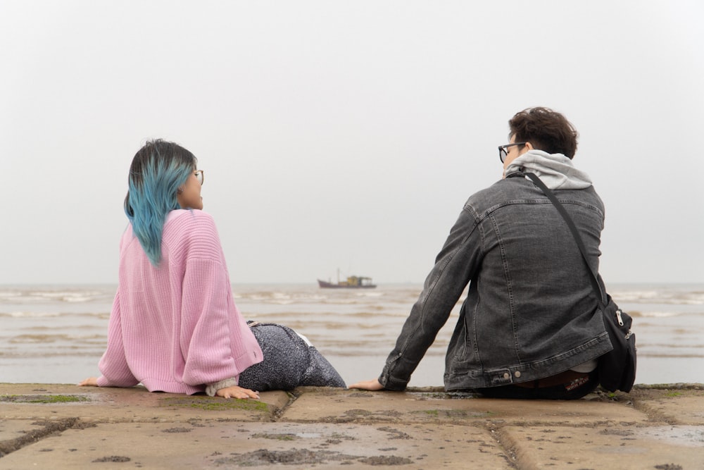 a man and a woman sitting on the edge of a pier