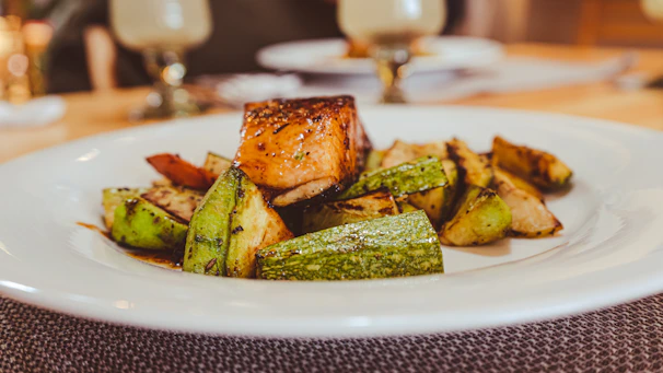 Close-up of a beautifully plated grilled salmon with a navy blue napkin and teak wood table background.
