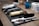 A neatly arranged set of barber tools on a wooden surface, including a gold-colored electric hair clipper, several combs, scissors, and a black brush. In the background, there are two rolls of white tissue and a blue bottle.