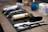A neatly arranged set of barber tools on a wooden surface, including a gold-colored electric hair clipper, several combs, scissors, and a black brush. In the background, there are two rolls of white tissue and a blue bottle.