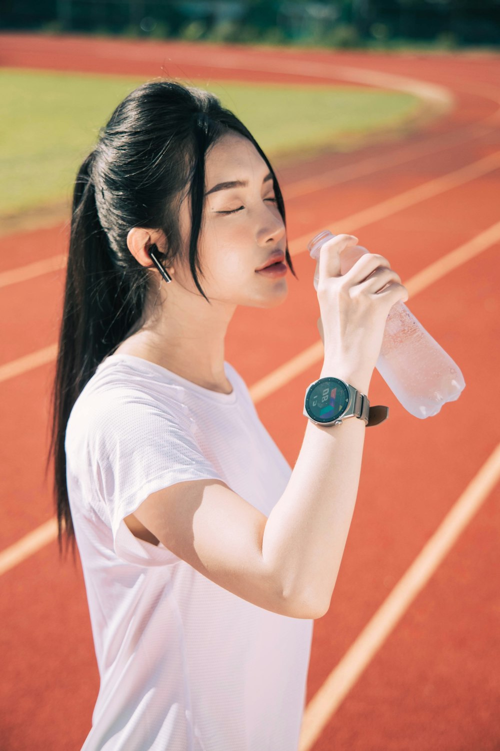 a woman drinking water while standing on a track
