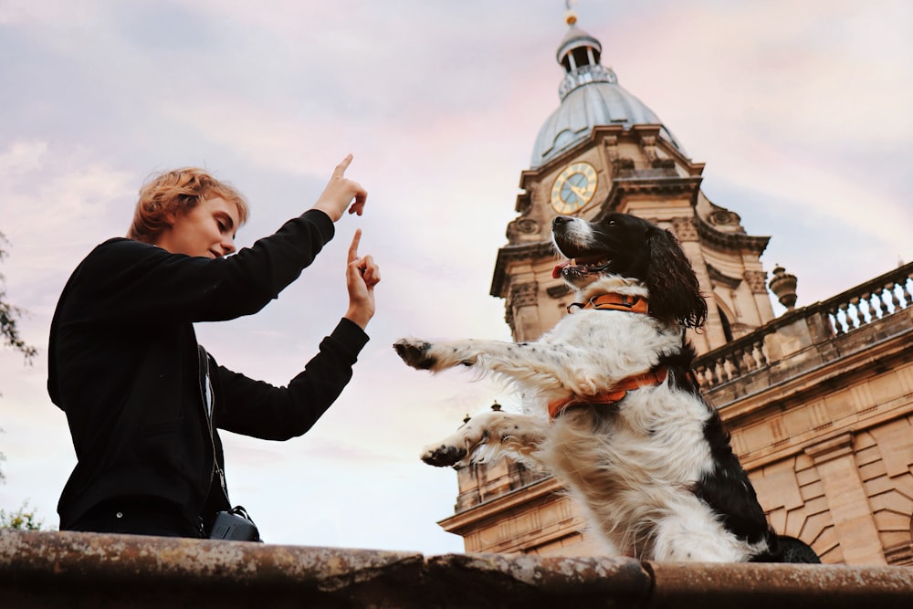 a woman pointing at a dog with a clock tower in the background