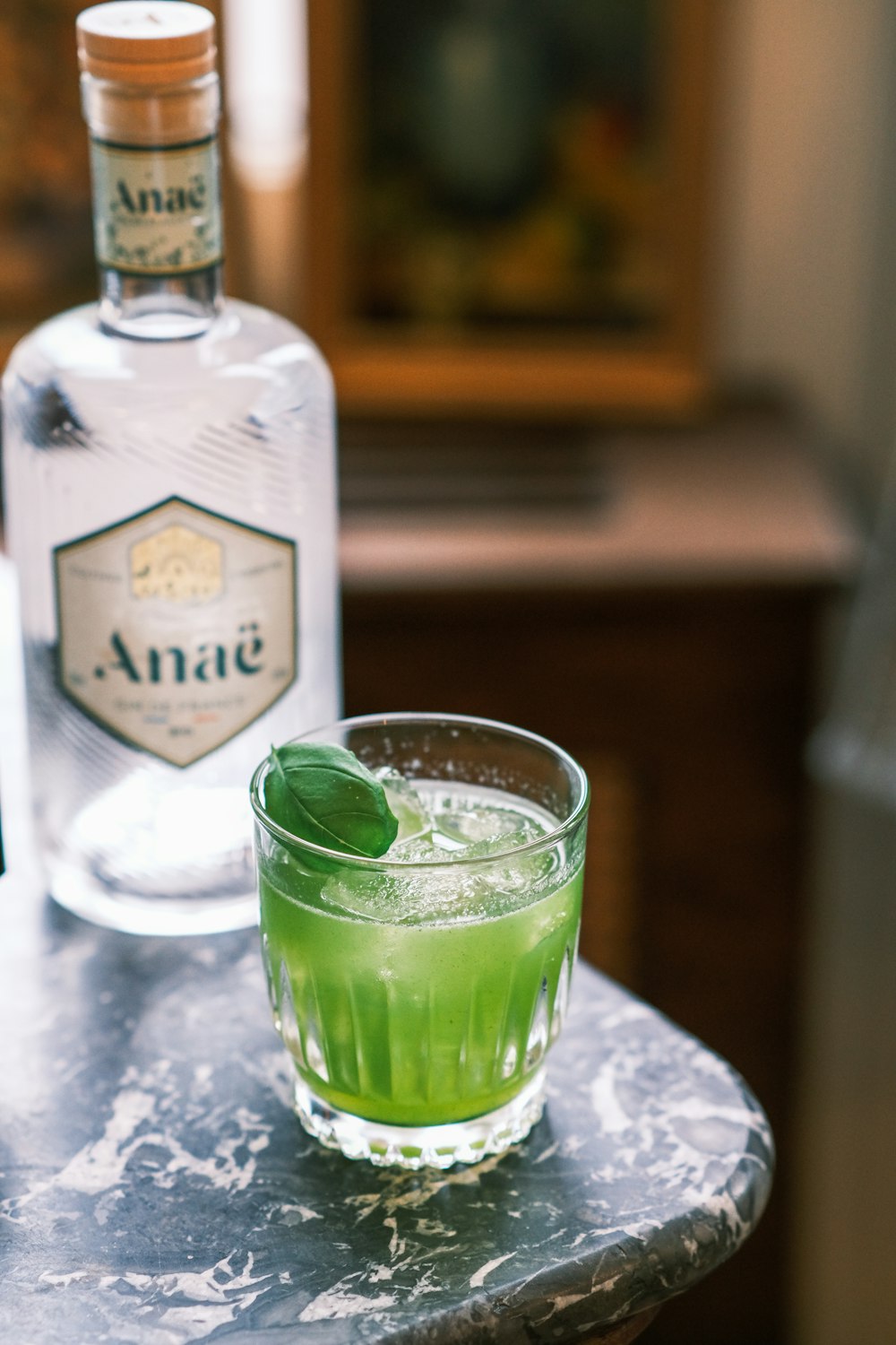 a glass of green liquid next to a bottle of gin