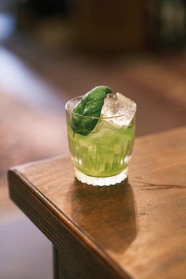 A vibrant bottle of green glow juice surrounded by fresh leafy greens and herbs on a rustic wooden table.