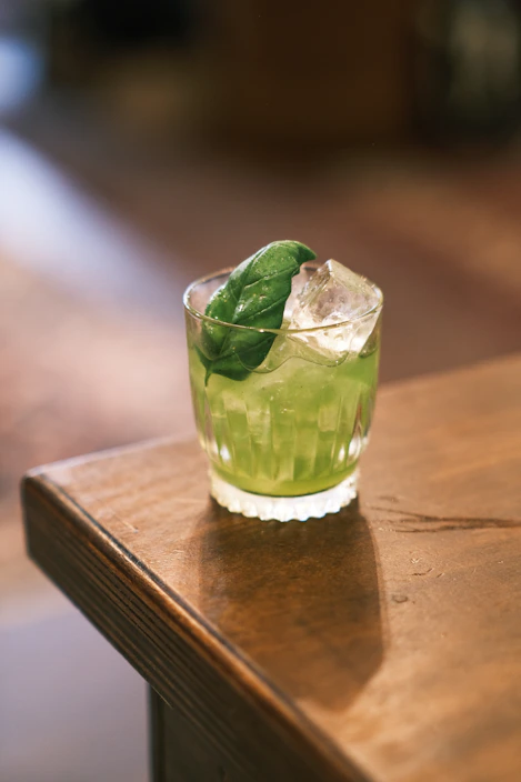 A vibrant bottle of green glow juice surrounded by fresh leafy greens and herbs on a rustic wooden table.