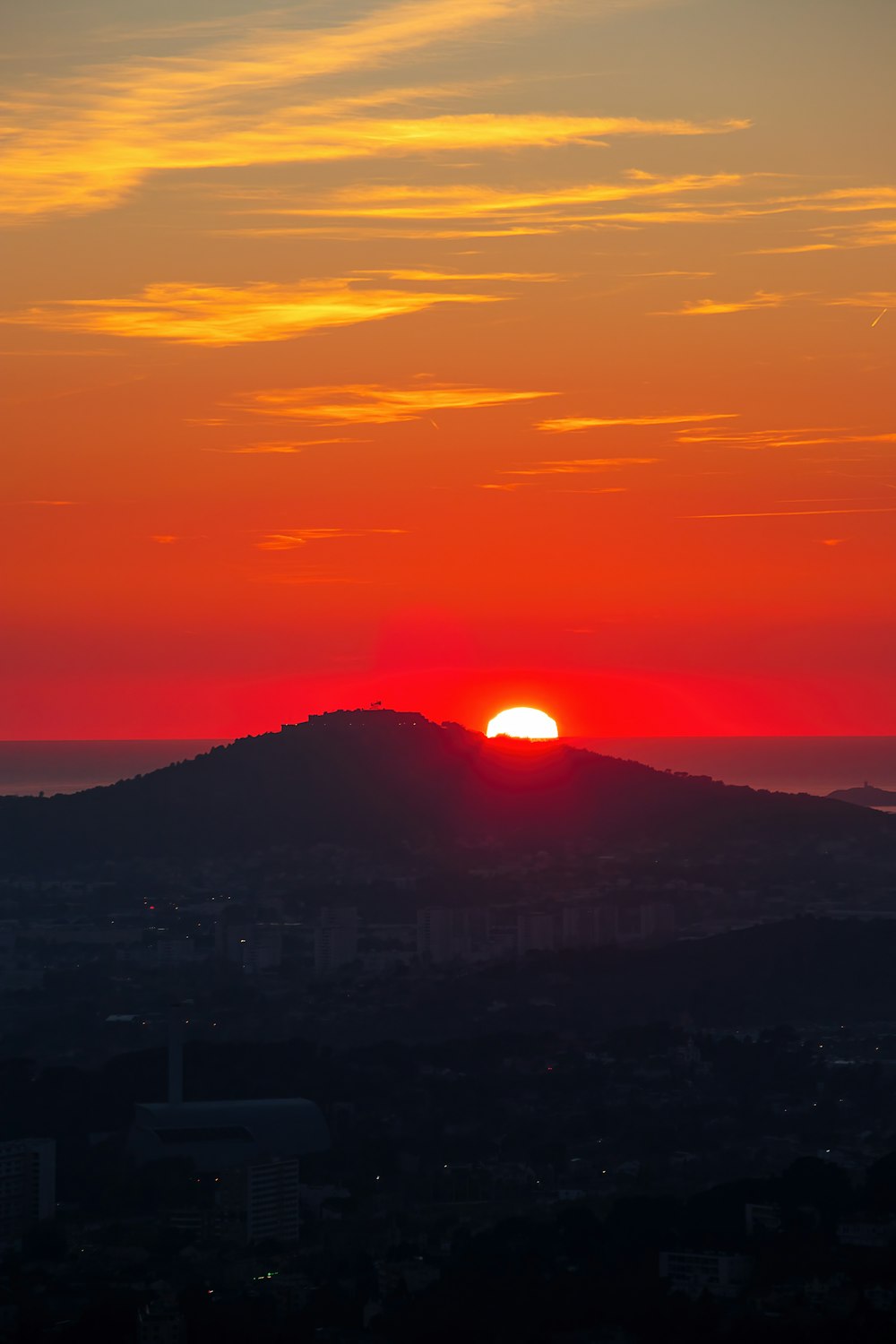 the sun is setting over a city with a mountain in the background