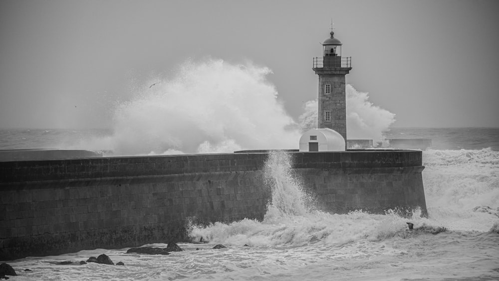 a black and white photo of waves crashing against a lighthouse