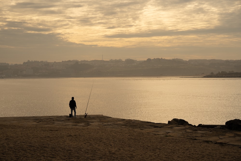 a man standing on top of a beach next to a body of water