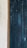 A close-up view of a textured surface featuring wooden vertical panels painted in a dark, weathered teal color. On the left, a small section of the wall with a rough, light-colored plaster finish is visible, bordered by a wooden frame.