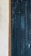 A close-up view of a textured surface featuring wooden vertical panels painted in a dark, weathered teal color. On the left, a small section of the wall with a rough, light-colored plaster finish is visible, bordered by a wooden frame.