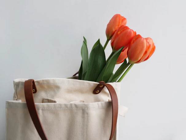 Close-up of a stylish canvas tote bag filled with fresh flowers against a bright background