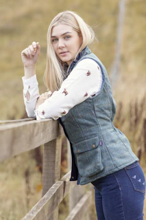 Julianna wearing a casual fall outfit with neutral tones, standing by a rustic wooden fence.
