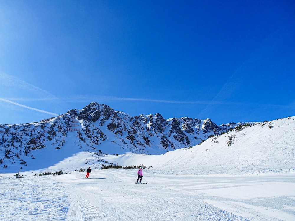 a couple of people riding skis down a snow covered slope