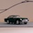 A classic miniature model car with a sleek design and dark green color is positioned on a simple, soft background. It features chrome detailing on the grille, wheels, and bumper, adding a vintage charm. The overall setting conveys a sense of elegance and nostalgia.
