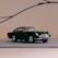 A classic miniature model car with a sleek design and dark green color is positioned on a simple, soft background. It features chrome detailing on the grille, wheels, and bumper, adding a vintage charm. The overall setting conveys a sense of elegance and nostalgia.