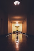 A dimly lit, vintage-style bowling alley with wooden lanes stretches into the distance. The lighting casts warm shadows, illuminating the smooth wooden floor and creating an intimate atmosphere. Bowling pins are lined up at the end of the lane, and a solitary bowling ball rests ready to be rolled.