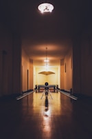 A dimly lit, vintage-style bowling alley with wooden lanes stretches into the distance. The lighting casts warm shadows, illuminating the smooth wooden floor and creating an intimate atmosphere. Bowling pins are lined up at the end of the lane, and a solitary bowling ball rests ready to be rolled.