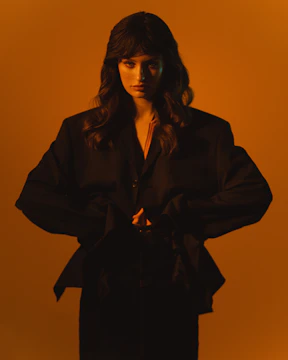 Model posing against a dark background with vibrant orange accents.