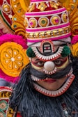 Close-up of a performer with vibrant face paint and feathered headdress smiling.