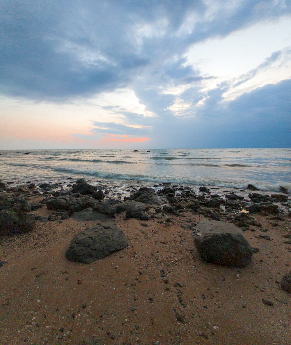 a beach with rocks and water under a cloudy sky