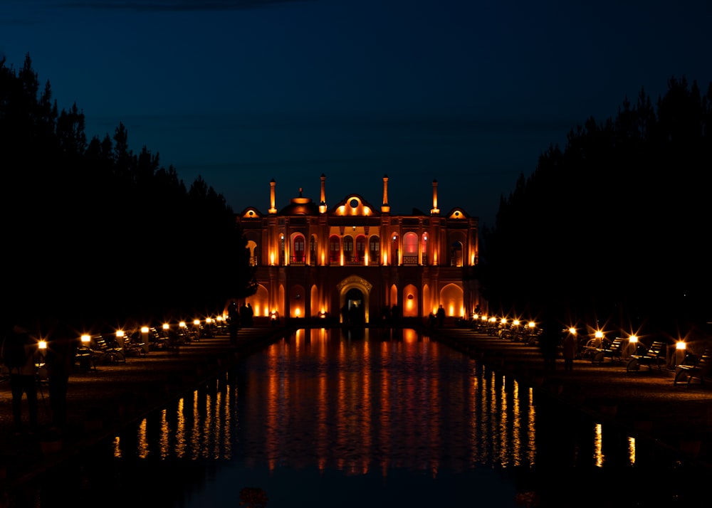 a large building lit up at night with lights reflecting in the water