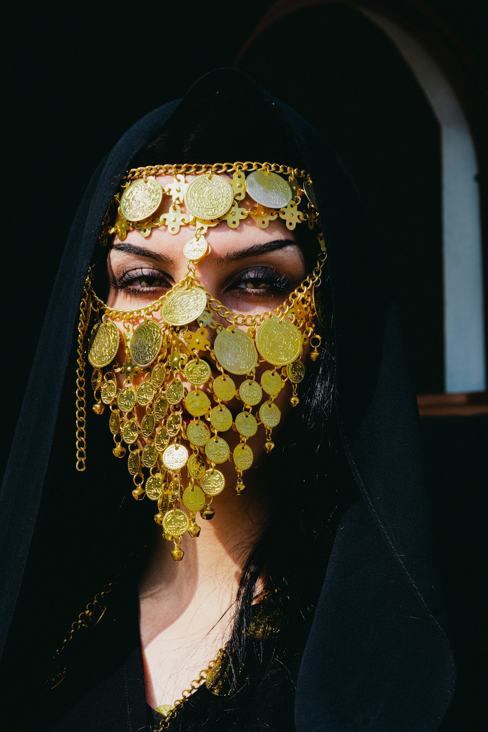 a woman in a black veil with gold coins on her face
