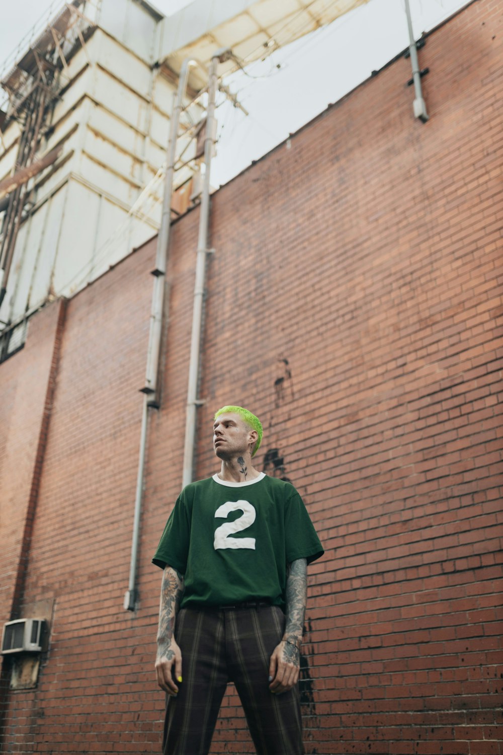 a man in a green shirt standing in front of a brick wall