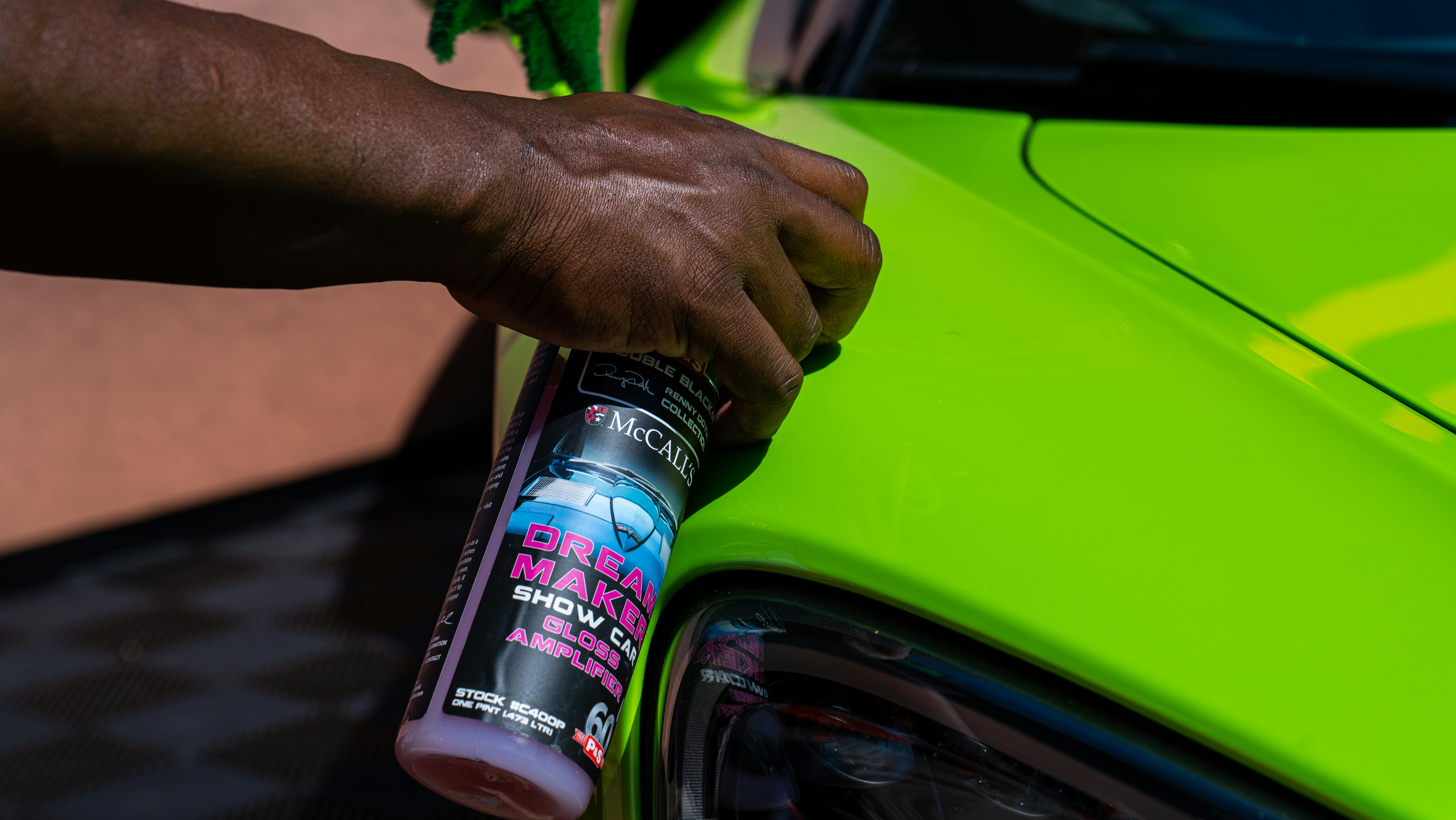 Detailer applying wax to dark green car in residential driveway