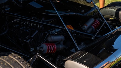 The image displays a detailed view of a car's suspension system, showcasing red coil springs and various mechanical components. A tire and parts of the vehicle's frame are visible, casting shadows on the reflective surfaces.