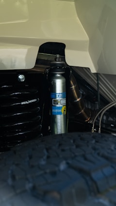 A close-up view of a Bilstein shock absorber mounted on a vehicle, revealing the company logo and various mechanical components. The tire tread is visible in the foreground, indicating this is part of a vehicle's suspension system.