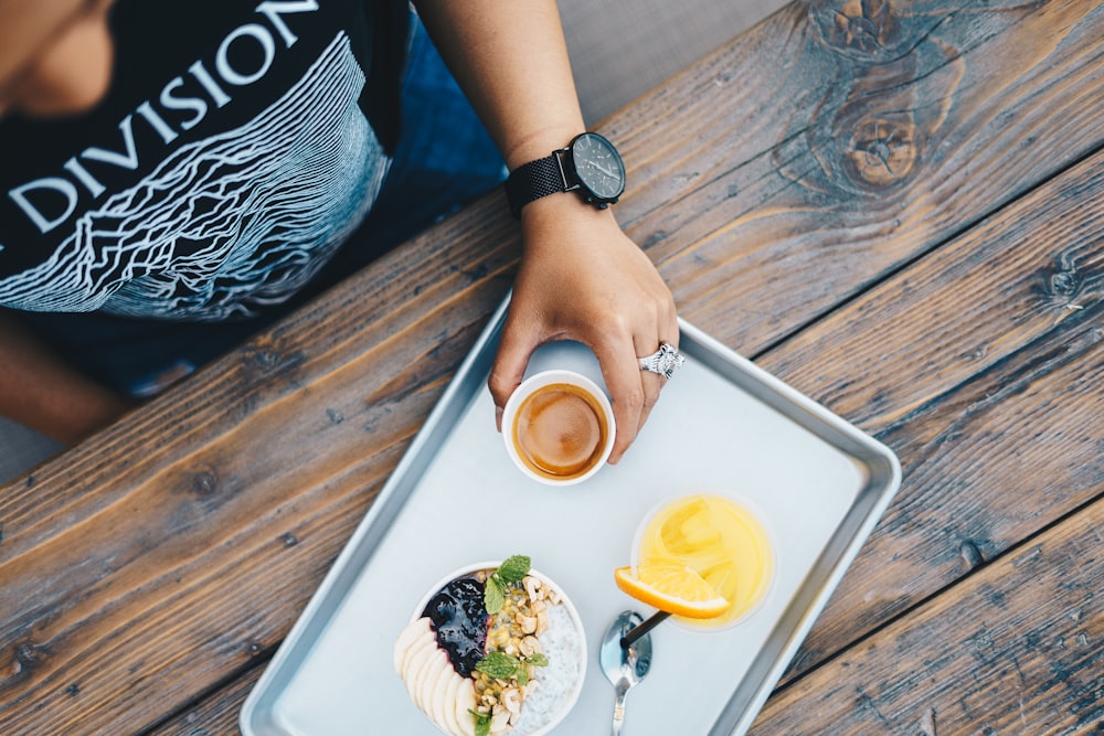 a person holding a cup of tea and a plate of food