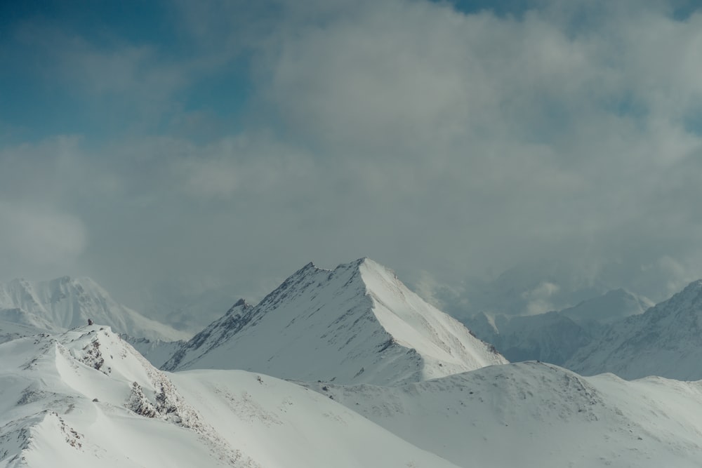 a mountain range covered in snow under a cloudy sky