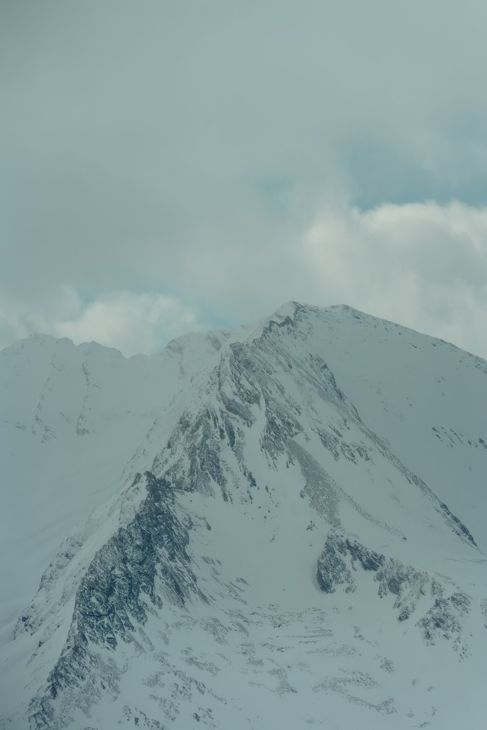 a mountain covered in snow under a cloudy sky