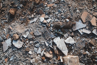 A collection of broken tiles, rocks, and stones scattered across the ground, creating a textured and chaotic surface. The debris is composed of various shapes and sizes, including pieces of ceramic and concrete.