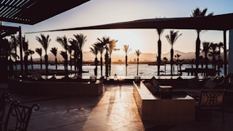 A cozy outdoor seating area by the villa's lagoon pool surrounded by tropical palm trees at sunset.