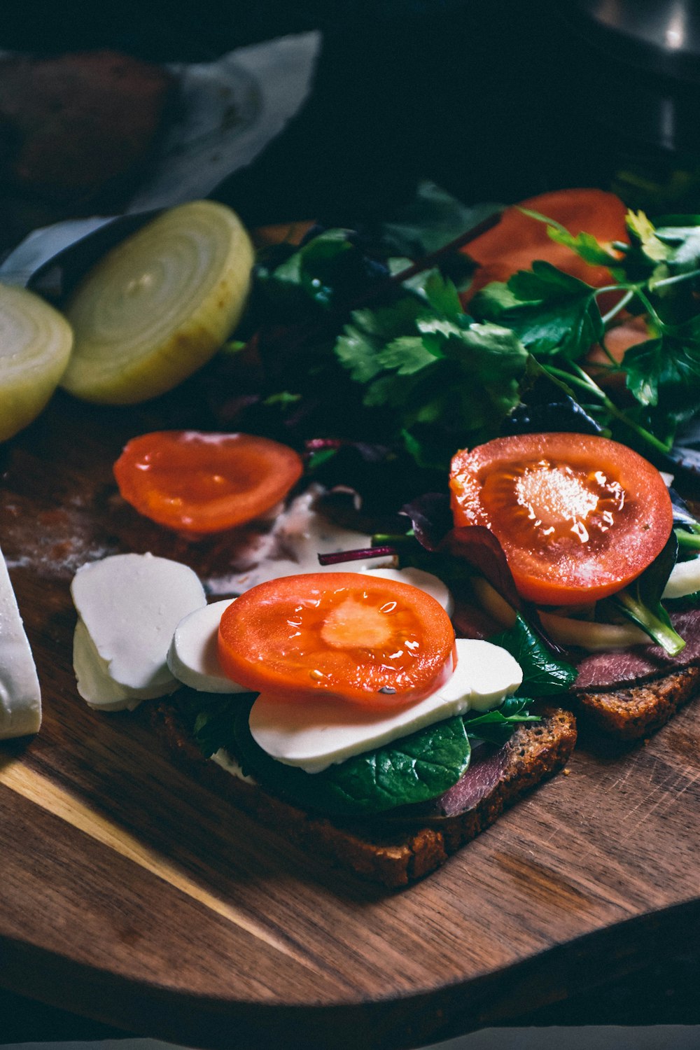 a wooden cutting board topped with a sandwich and veggies