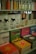 Various bottles of cleaning products are neatly organized on shelves, accompanied by colorful books with travel-themed covers. The upper shelf features sleek bottles with liquids in different hues, while the lower shelf displays vibrant books with titles such as 'Tulum', 'Bali', and 'Jaipur'. The arrangement suggests a boutique or specialty store layout.