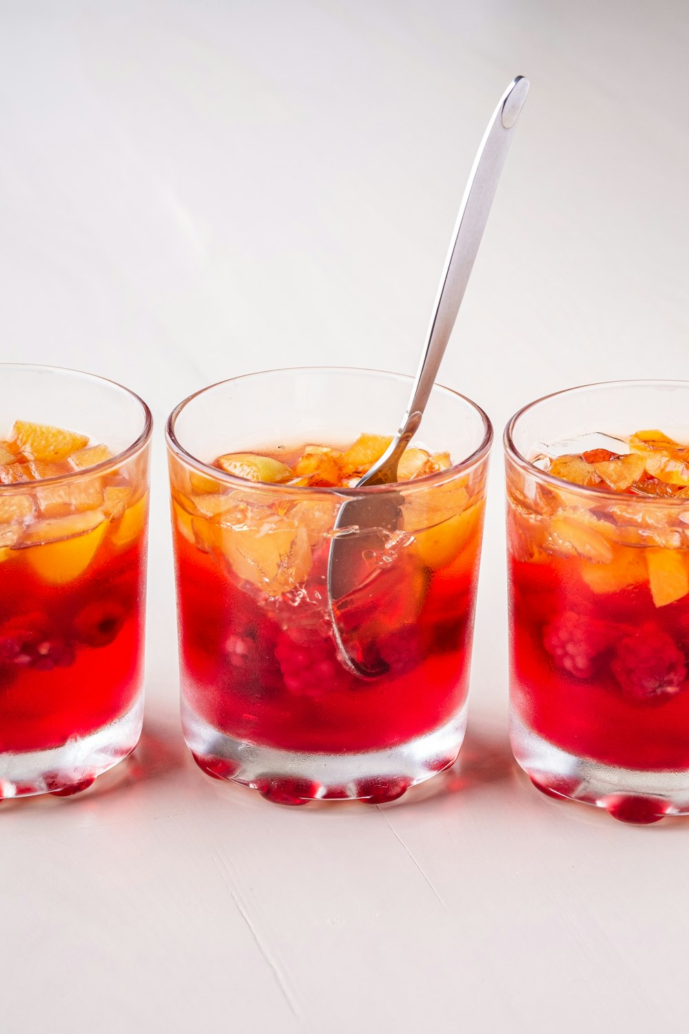 three glasses filled with fruit and a spoon