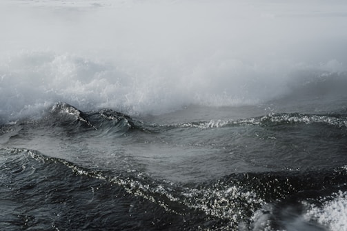 Dark, turbulent ocean waves crash beneath a misty sky, creating a moody and dramatic seascape.